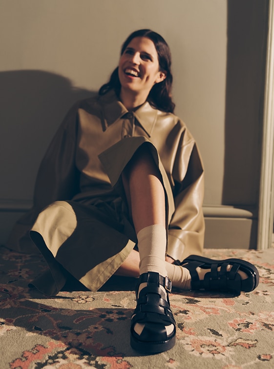 Woman sitting on floor wearing black leather Russell and Bromley fisherman sandals; Petra